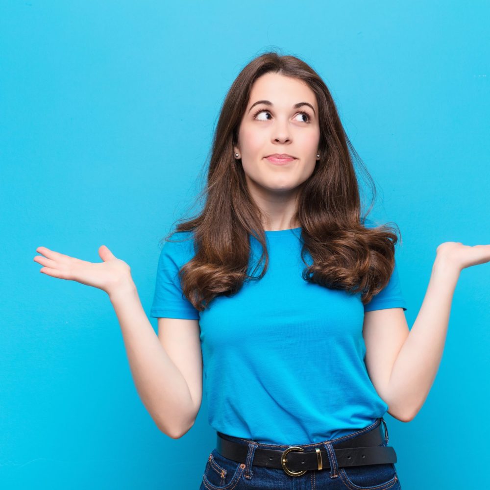 young pretty woman feeling puzzled and confused, doubting, weighting or choosing different options with funny expression against blue wall